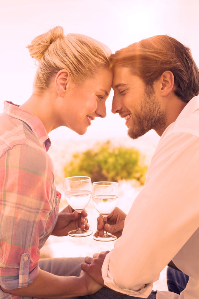 Happy young couple sitting in the garden enjoying wine together on a sunny day